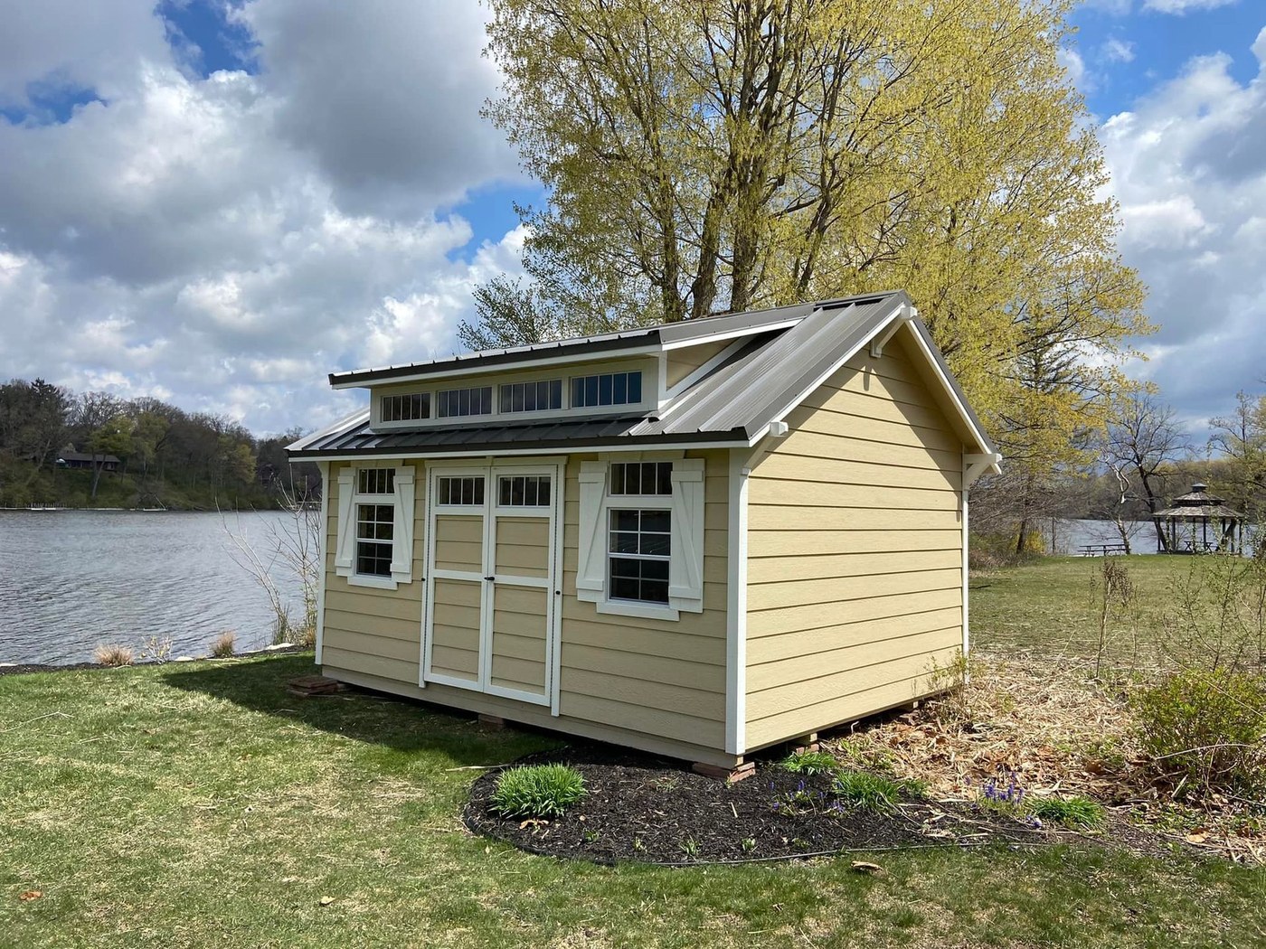 A cream garden shed with a dormer by a lake