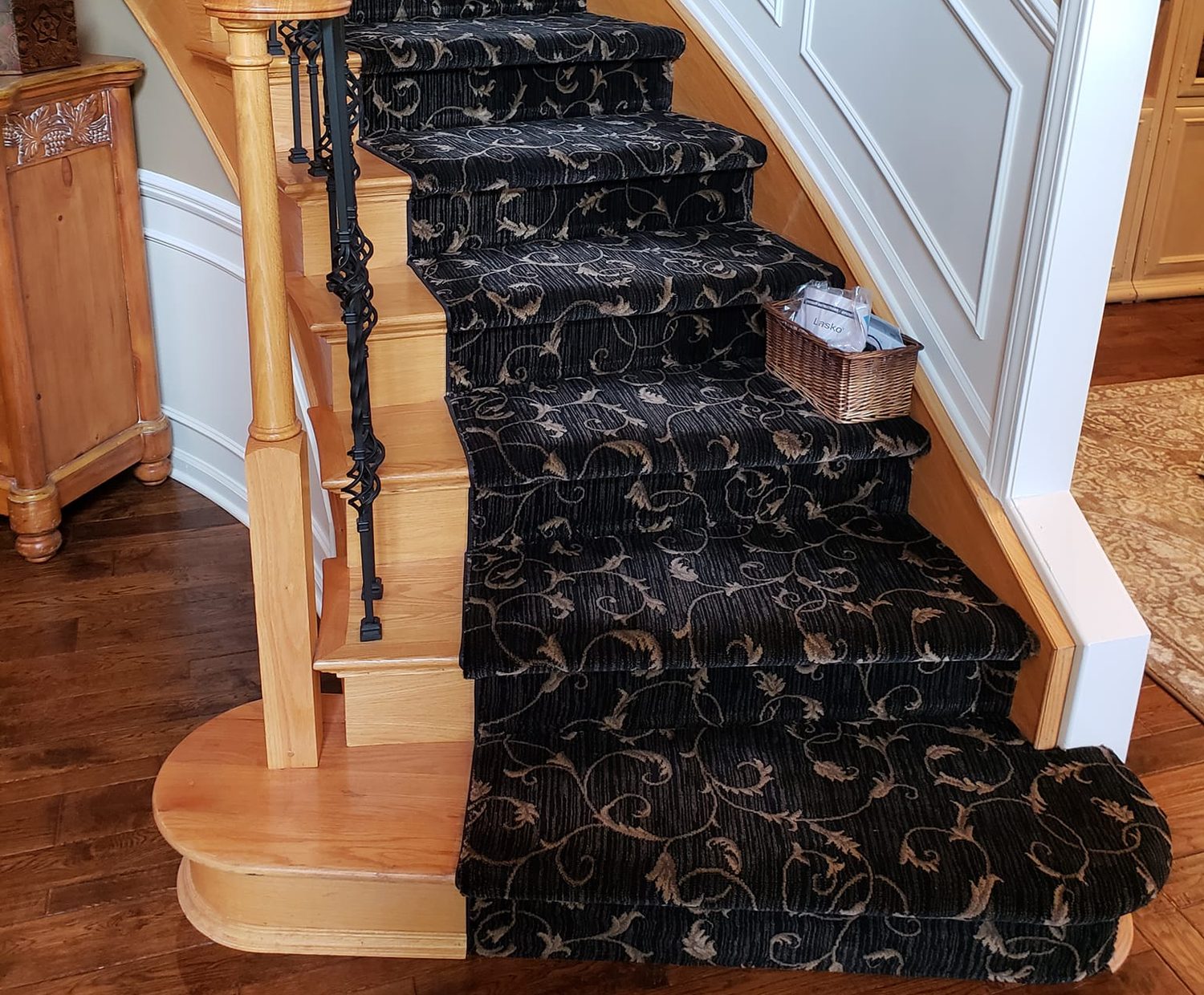 A curved oak staircase carpeted by Cut a Rug in a black and gold scroll-pattern runner