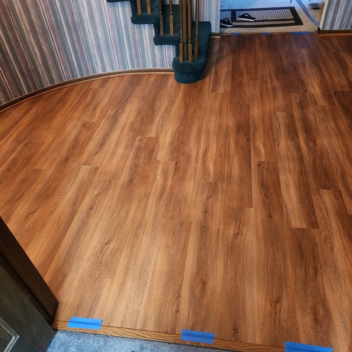 A warm brown plank floor curving around the foot of a staircase