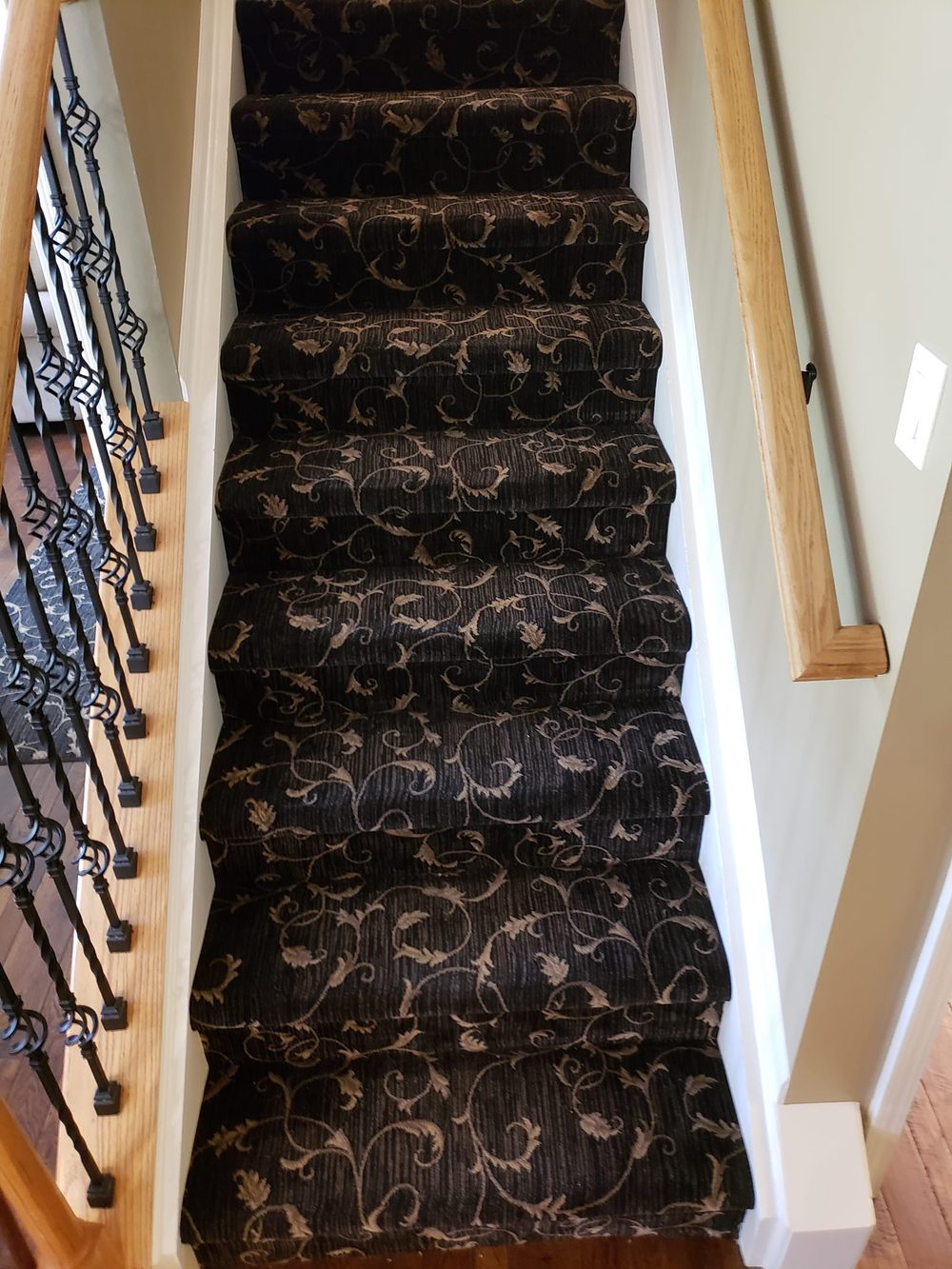 Looking down a straight stair carpeted in black patterned carpet