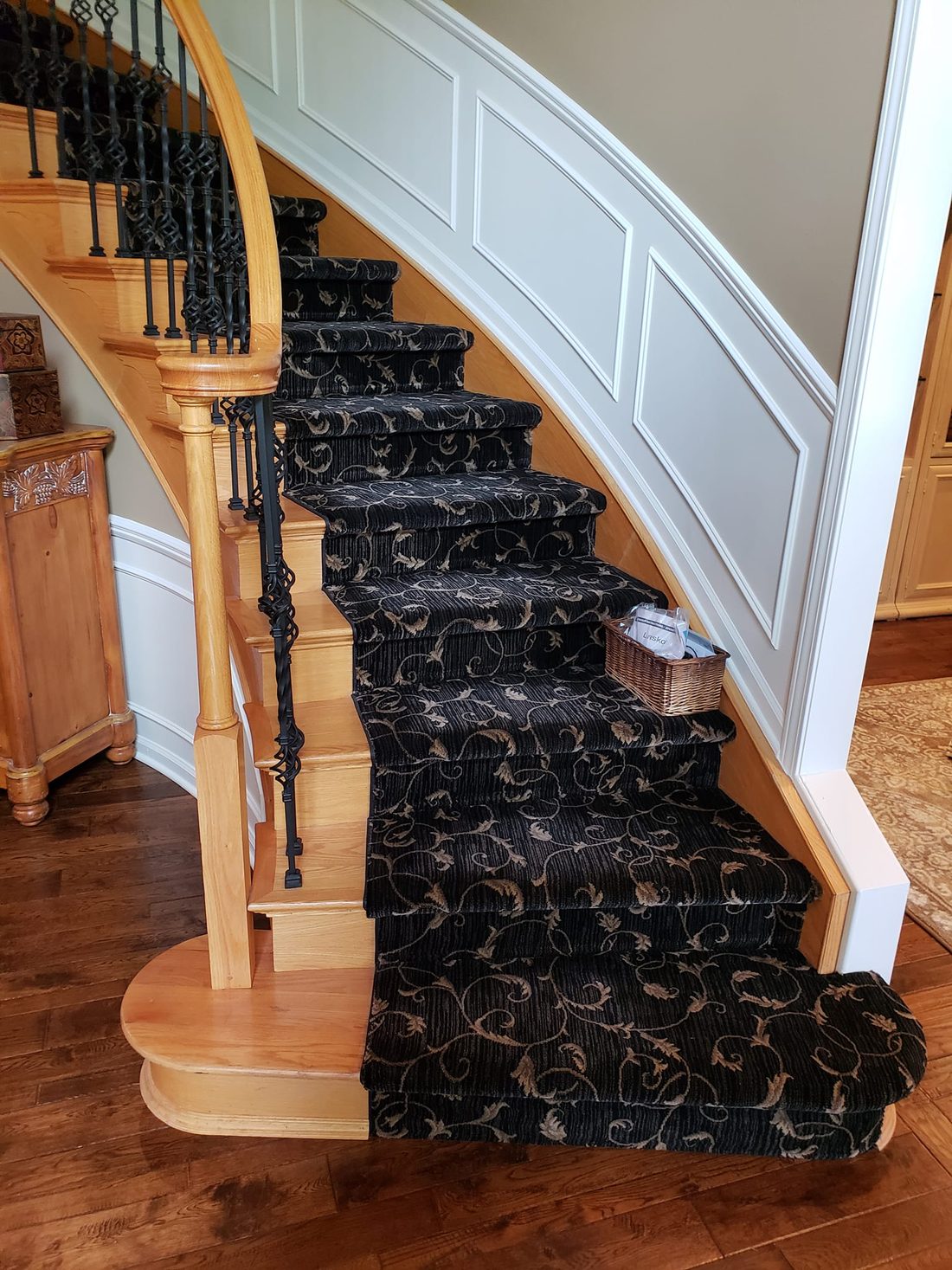 A curved staircase carpeted in a black and gold scroll-pattern runner
