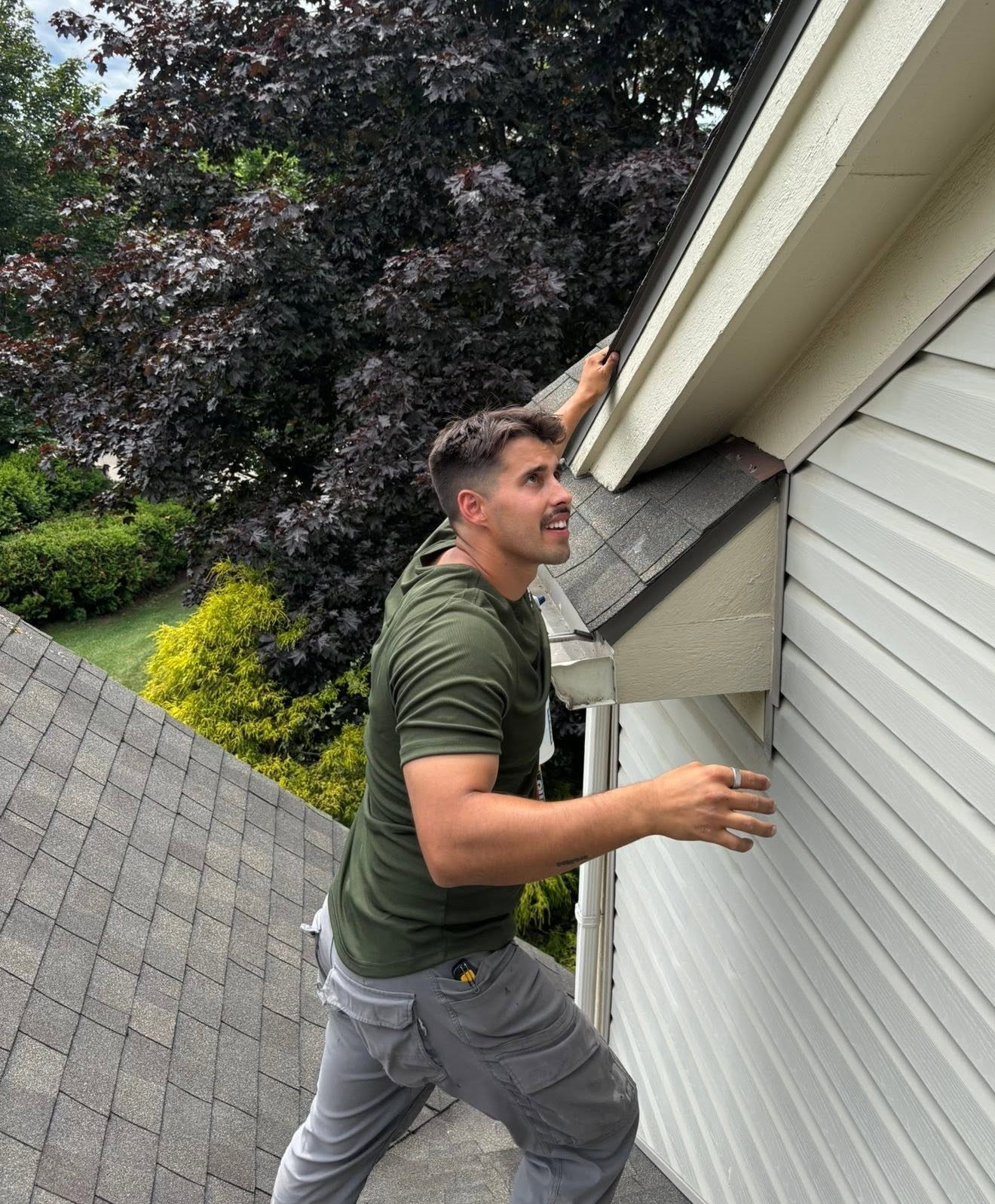 Nick from FenGuard on a roof, reaching up to check the soffit and eave of a house