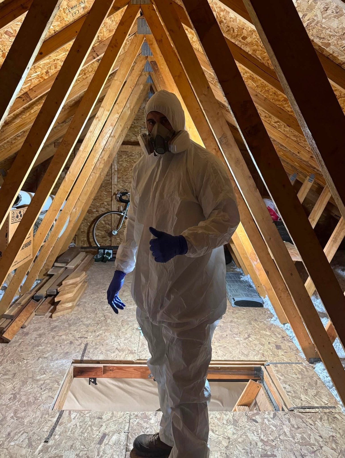 Nick in a protective suit and respirator standing in an unfinished attic