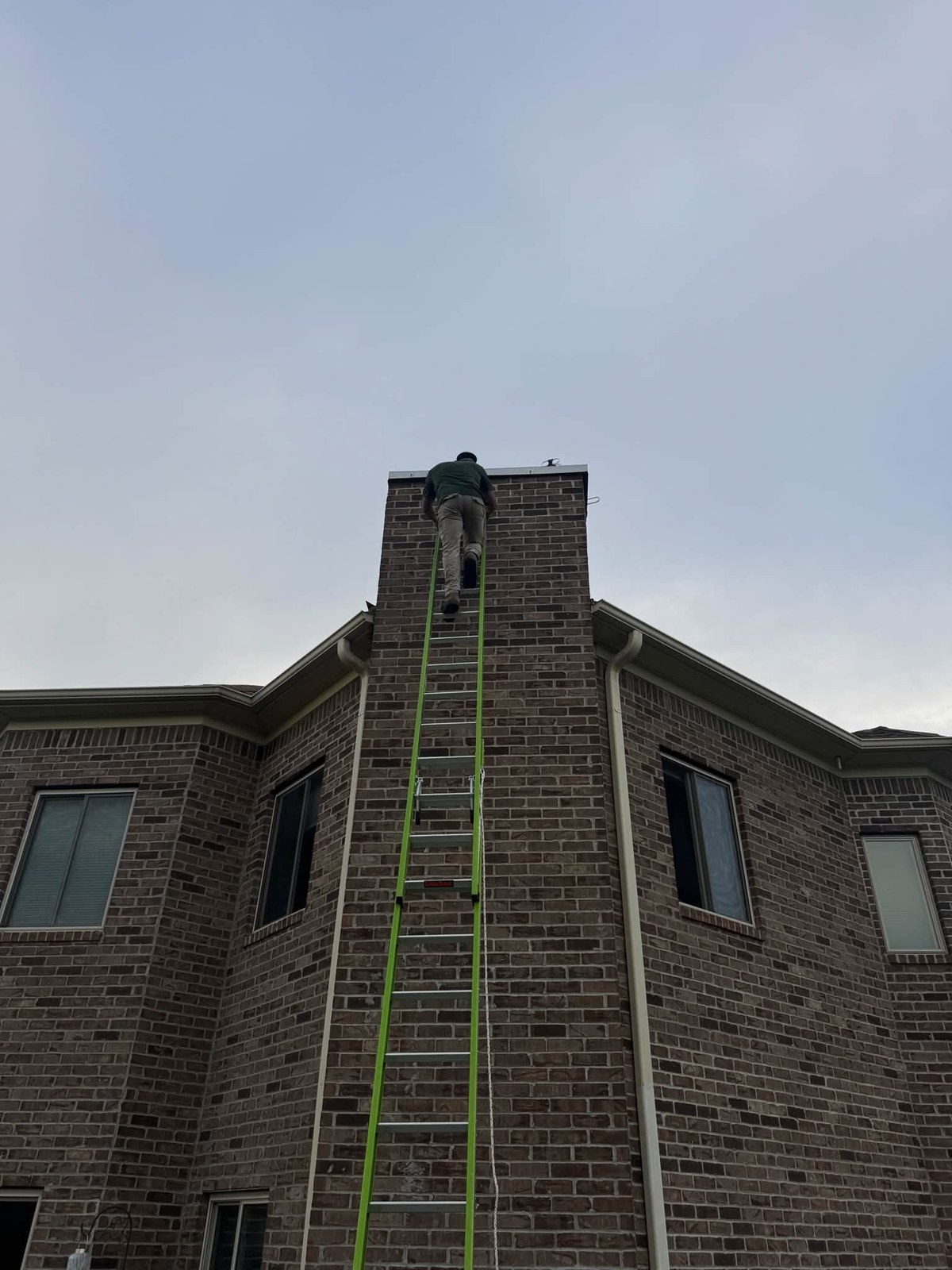 A ladder run up a tall brick chimney with Nick at the top