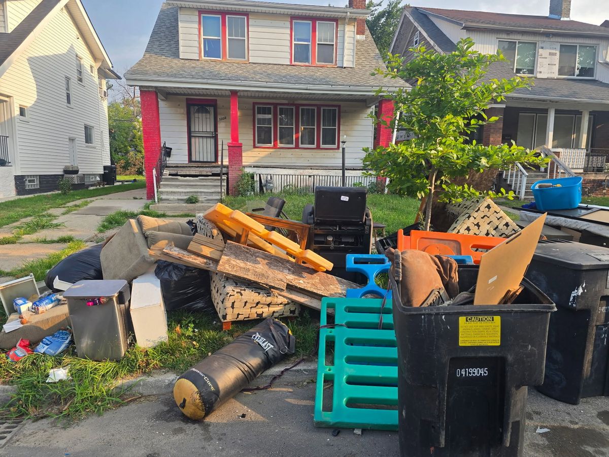 A pile of household junk, pallets and bins at the curb in front of a house
