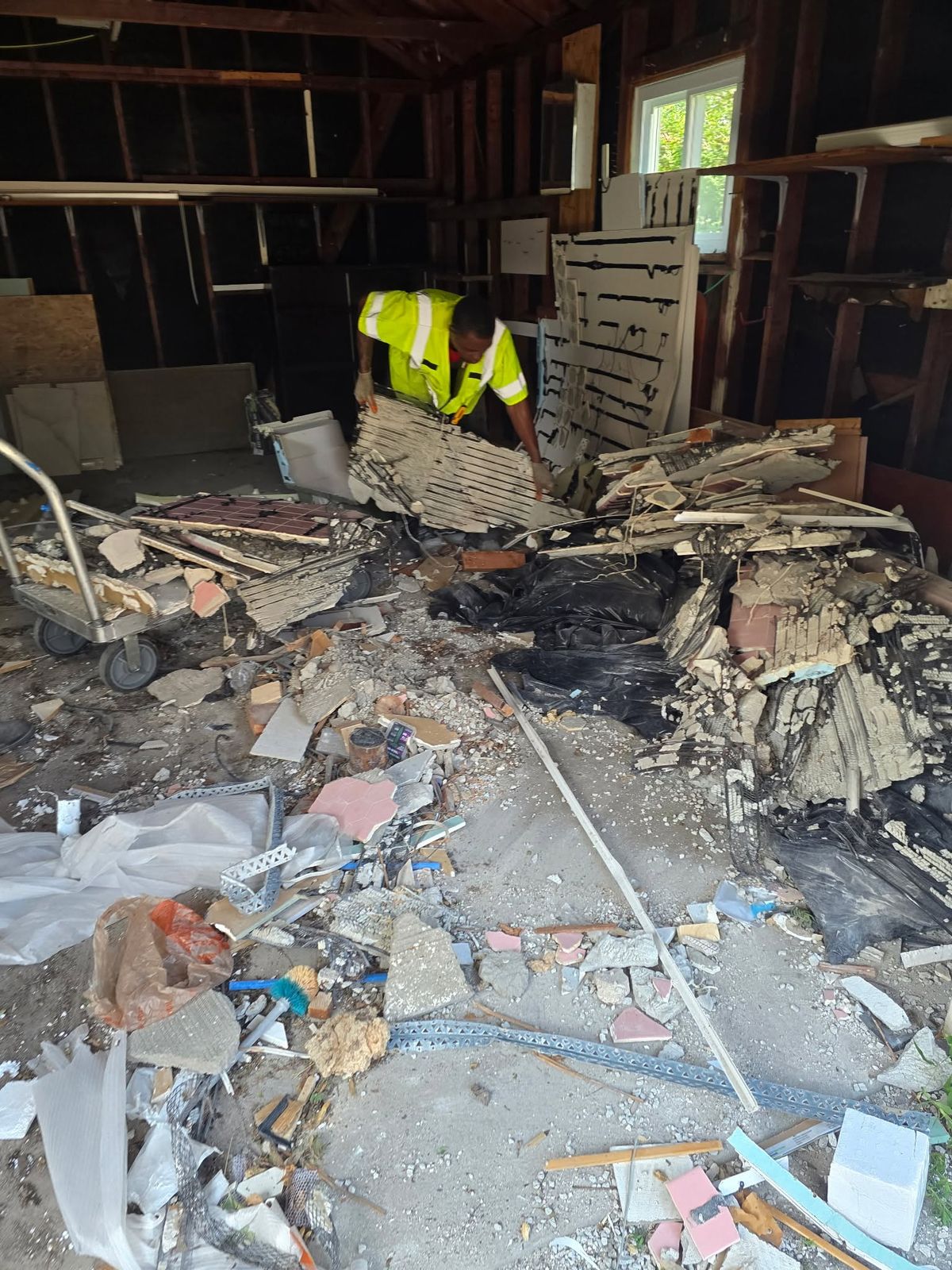 A crew member in a safety vest clearing construction debris from a garage