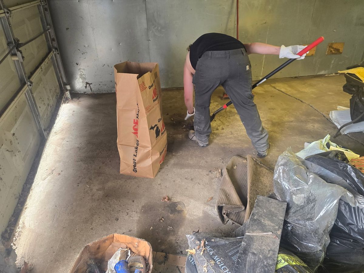 A crew member sweeping a garage floor beside bagged debris
