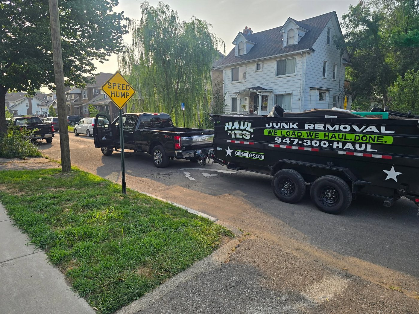 The Haul Yes truck and black dump trailer parked outside a house, lettered Junk Removal, We Load We Haul Done, 947-300-HAUL