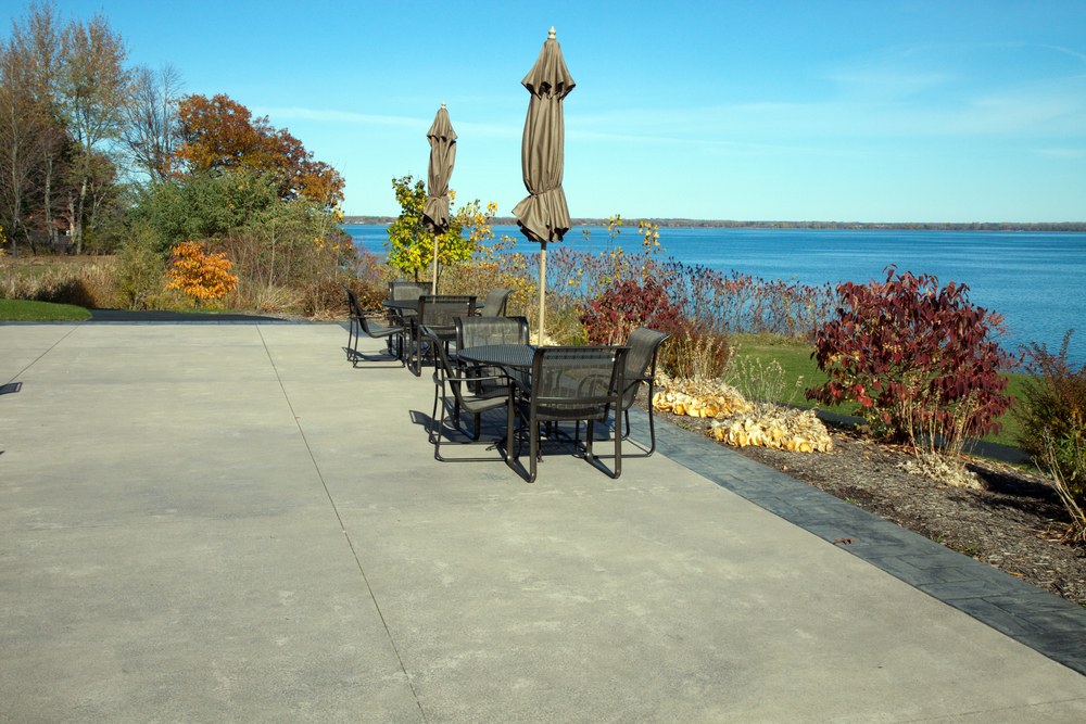 A large concrete patio with tables and umbrellas overlooking a lake