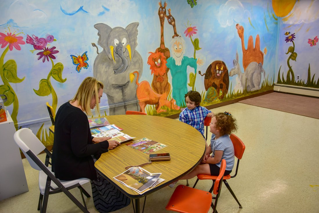 A teacher reading with children in the classroom with the jungle mural